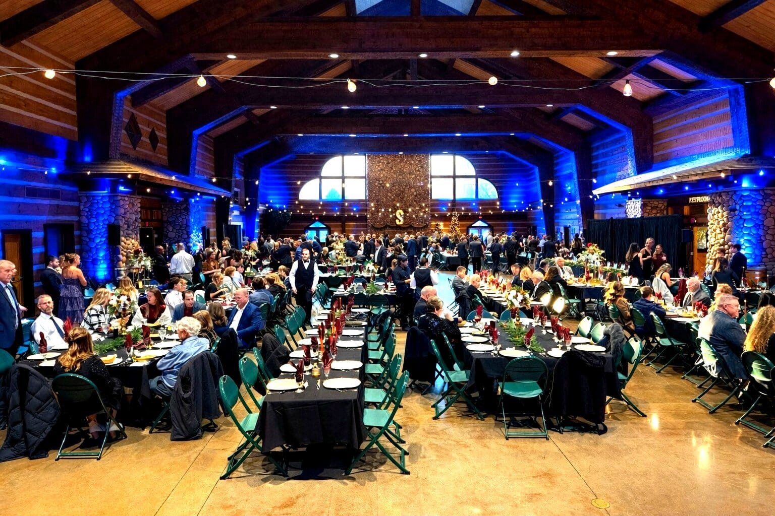 Wide view of a Discovery Lodge wedding reception with black-linen tables, log walls and blue uplighting