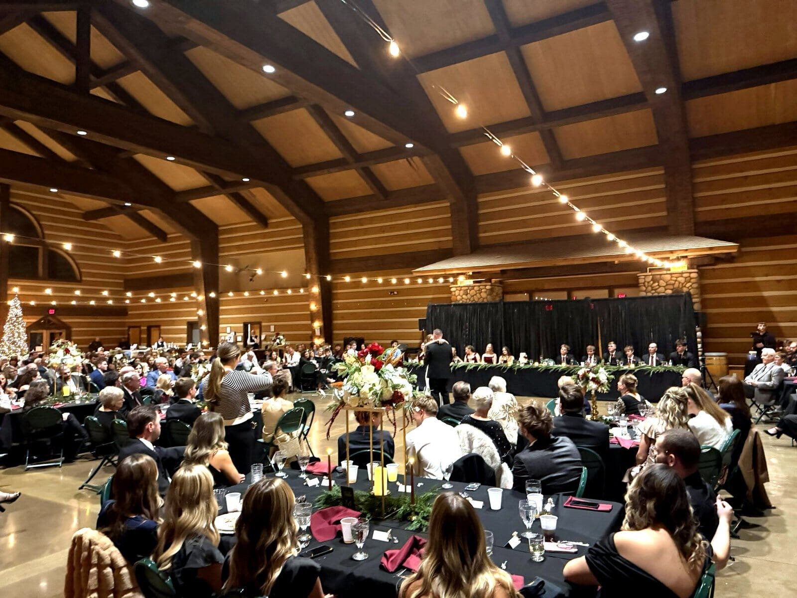 Guests at black-linen tables under string lights during a speech at a Discovery Lodge wedding reception
