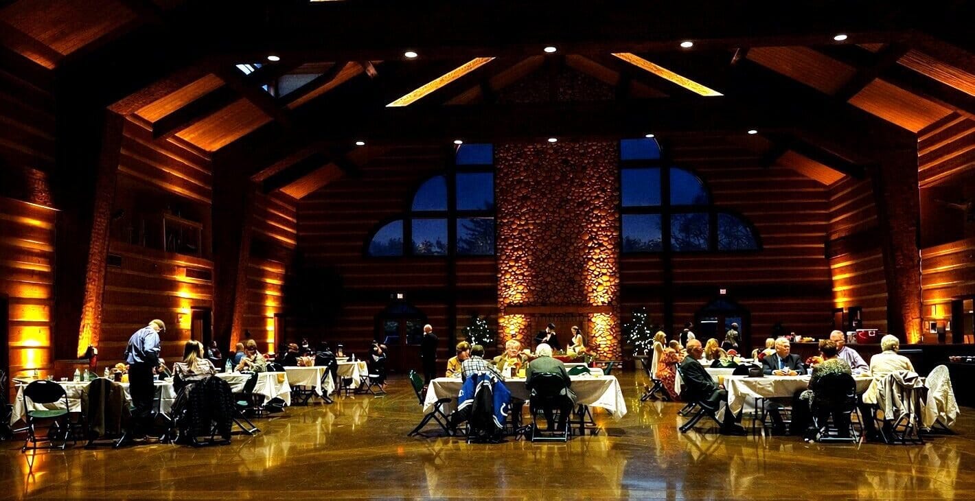 Discovery Lodge reception room in Evansville, Indiana, with log walls, high beamed ceiling, stone fireplace column and warm amber uplighting
