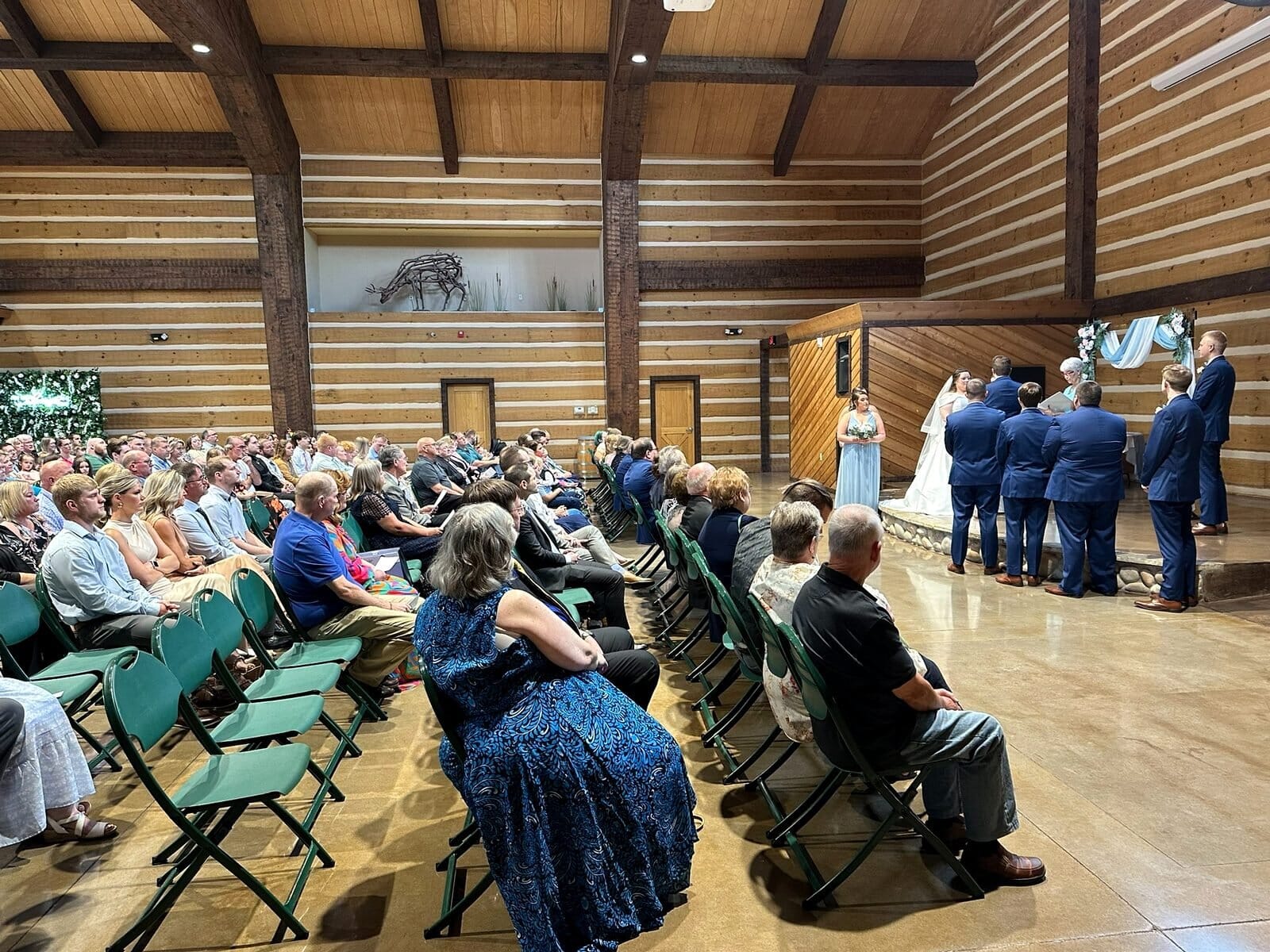 Indoor wedding ceremony at Discovery Lodge in Evansville with guests seated in rows facing the couple at the stone fireplace end of the room