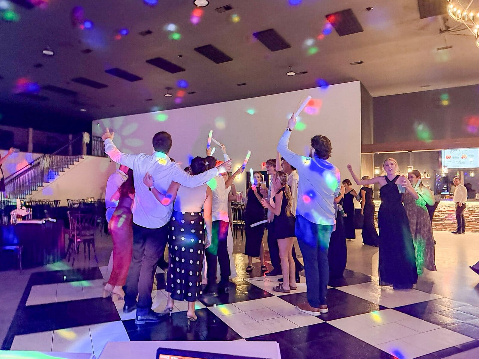 Guests dancing on a packed checkered dance floor with glow sticks at a Highbanks wedding reception.
