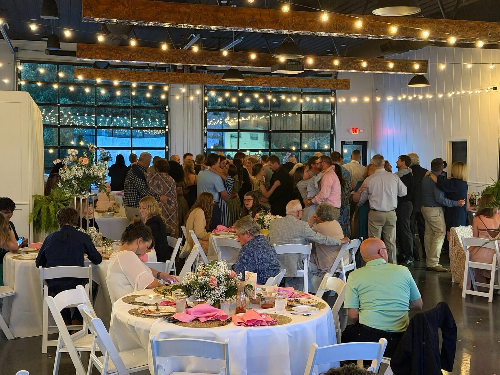 Guests at round tables during a wedding reception in Event Barn A at Mahr Park Arboretum, under wood beams and string lights