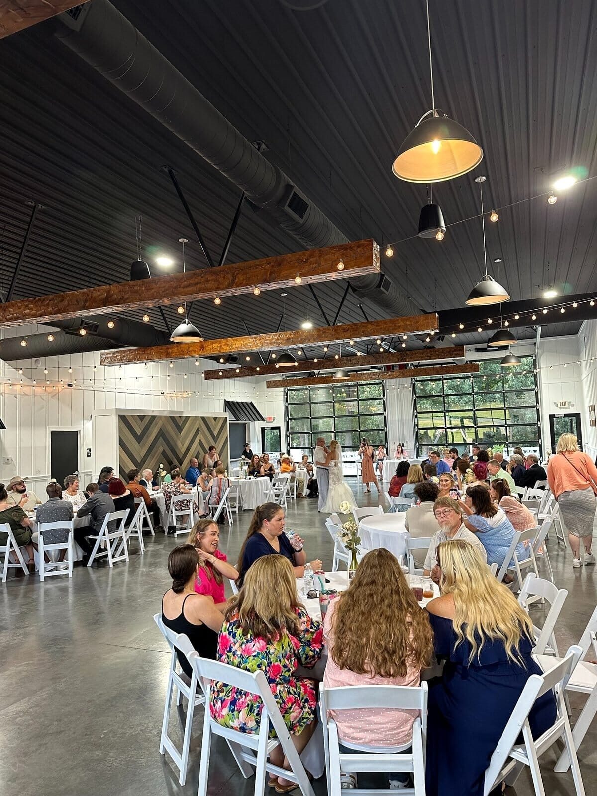 Wedding reception inside Event Barn A at Mahr Park Arboretum in Madisonville, Kentucky, with wood beams, string lights and glass roll-up doors