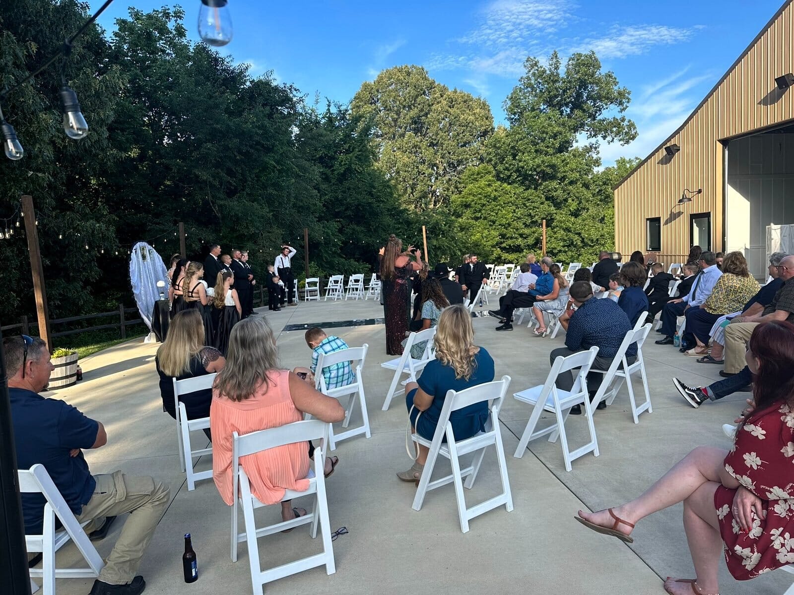 Outdoor wedding ceremony on the concrete patio beside the Event Barn at Mahr Park Arboretum, guests in white folding chairs