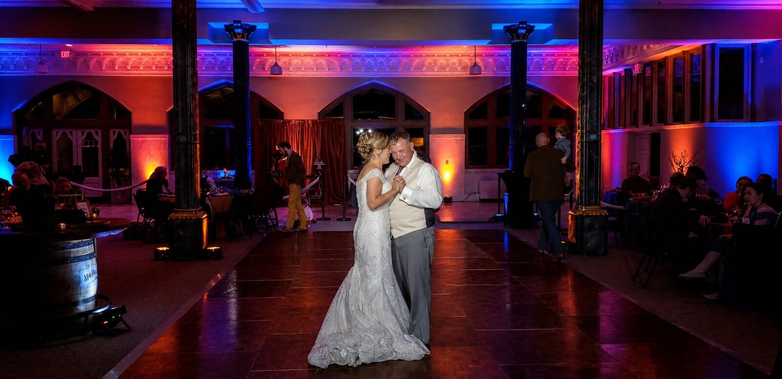 Bride and groom sharing their first dance in the long columned hall of The Old Post Office in Evansville, with colored uplighting on the walls