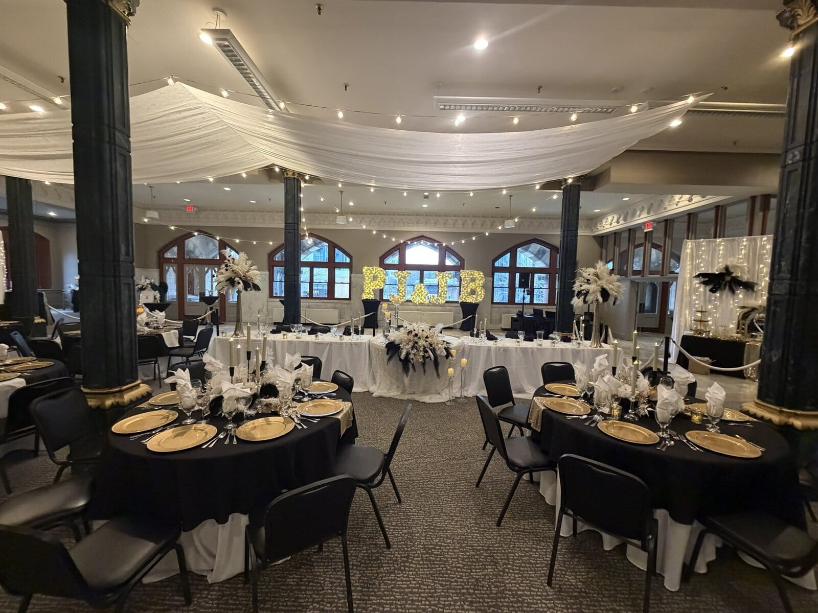 The Old Post Office ballroom in Evansville set for a wedding reception, with dark columns, tall arched windows, draped ceiling fabric and string lights over the head table