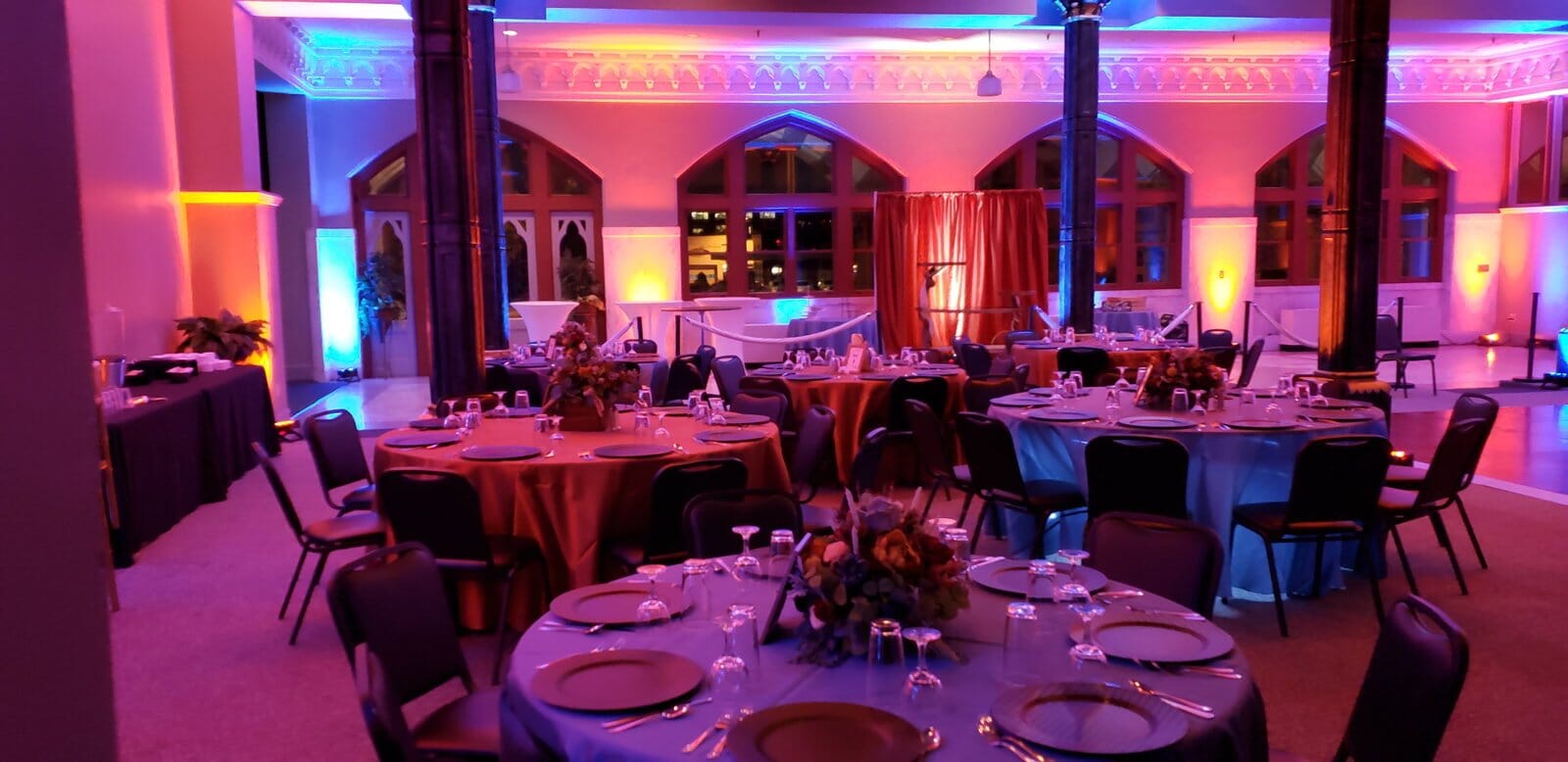 Reception tables at The Old Post Office in Evansville with red and blue uplighting on the walls and arched windows