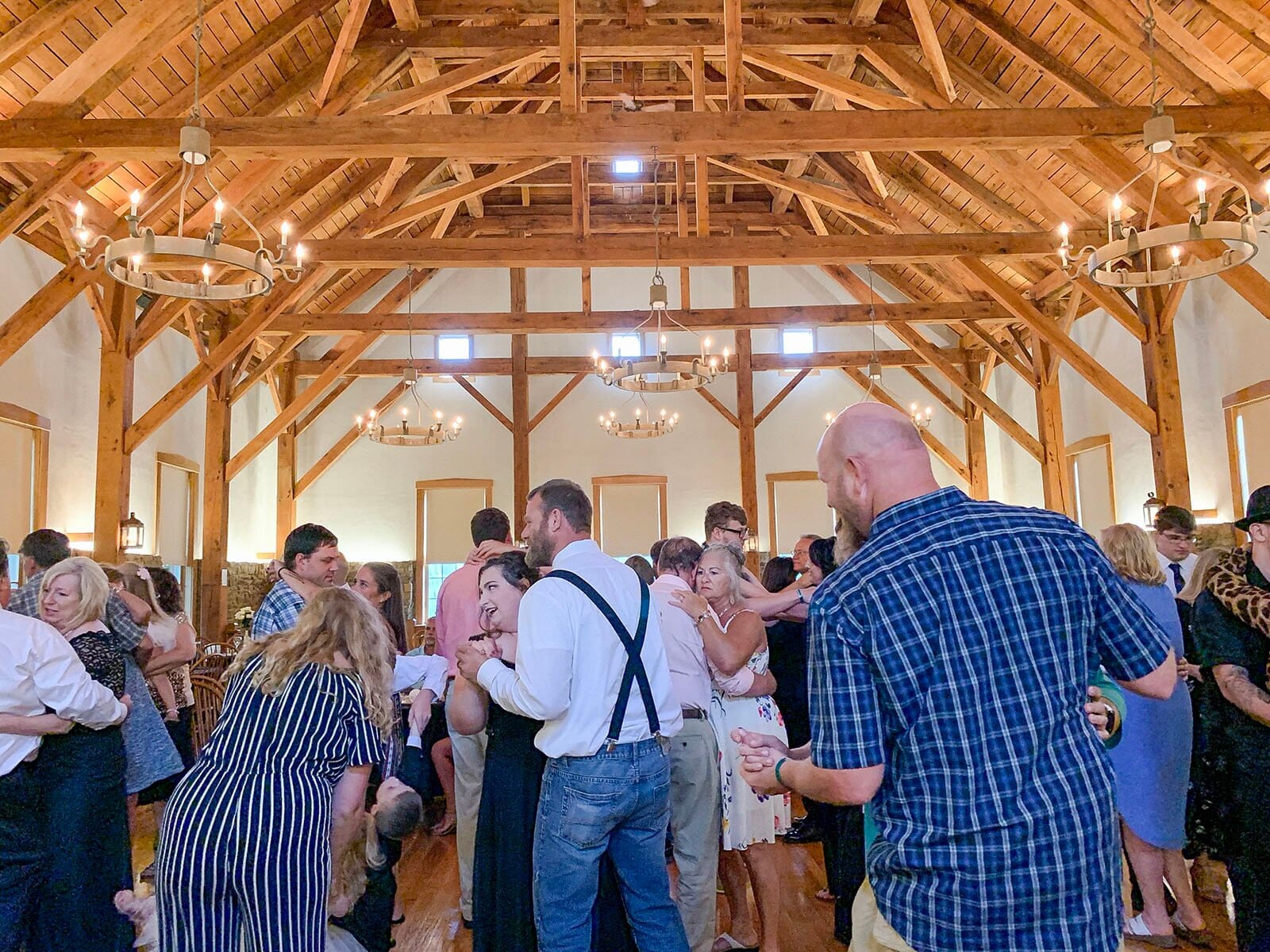 Packed dance floor at a Rapp-Owen Granary wedding reception, with exposed timber trusses and chandeliers overhead