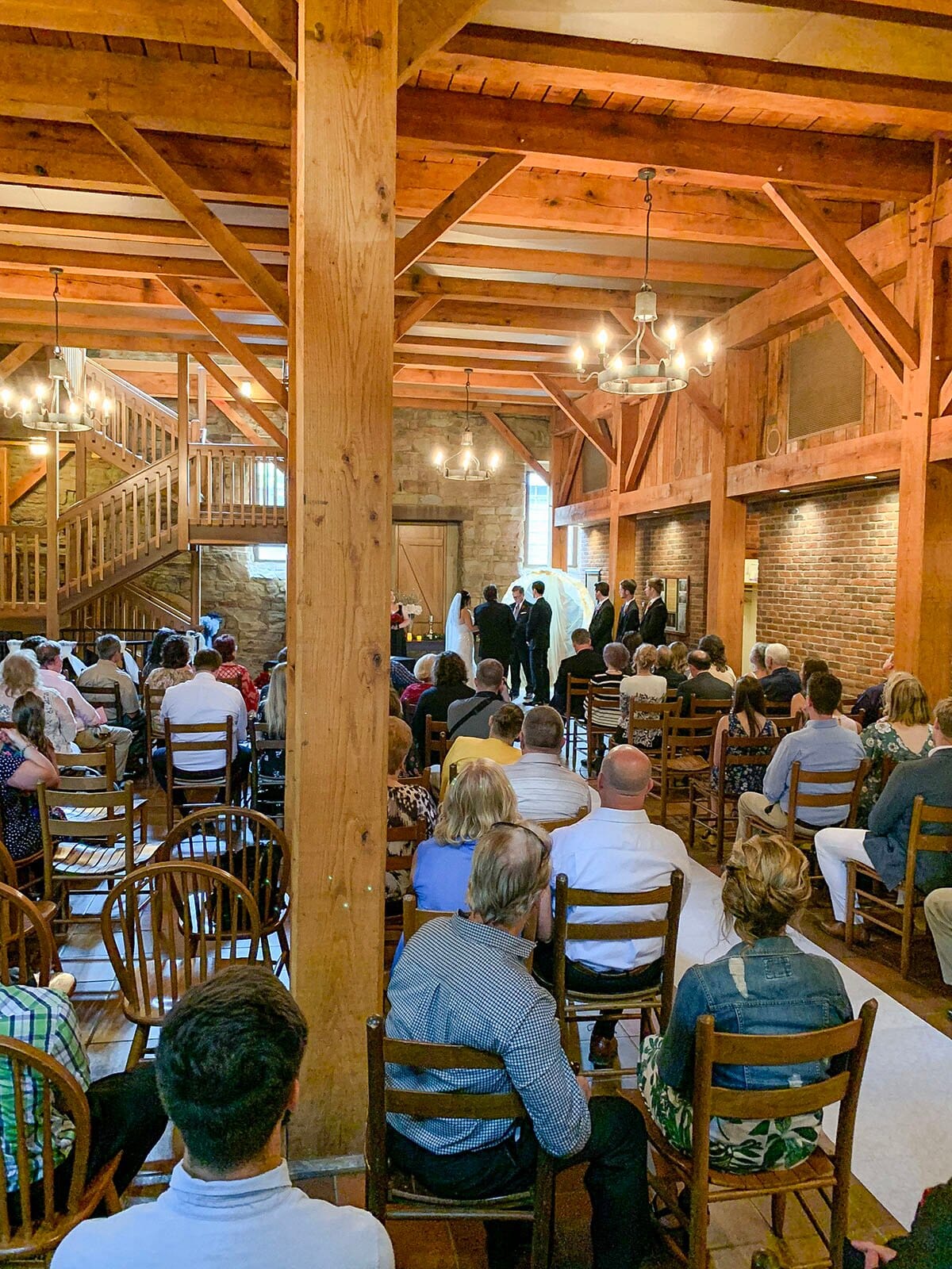 Guests seated in wooden chairs for an indoor wedding ceremony inside the Rapp-Owen Granary, with brick walls and timber beams